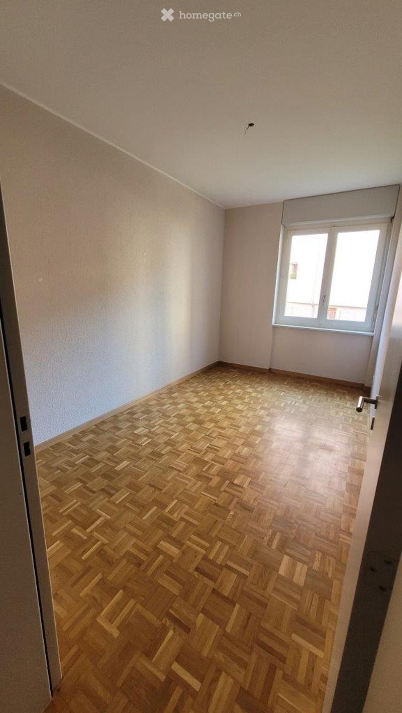 Empty room with wooden herringbone flooring, white walls, and a single window with white frame and blinds.