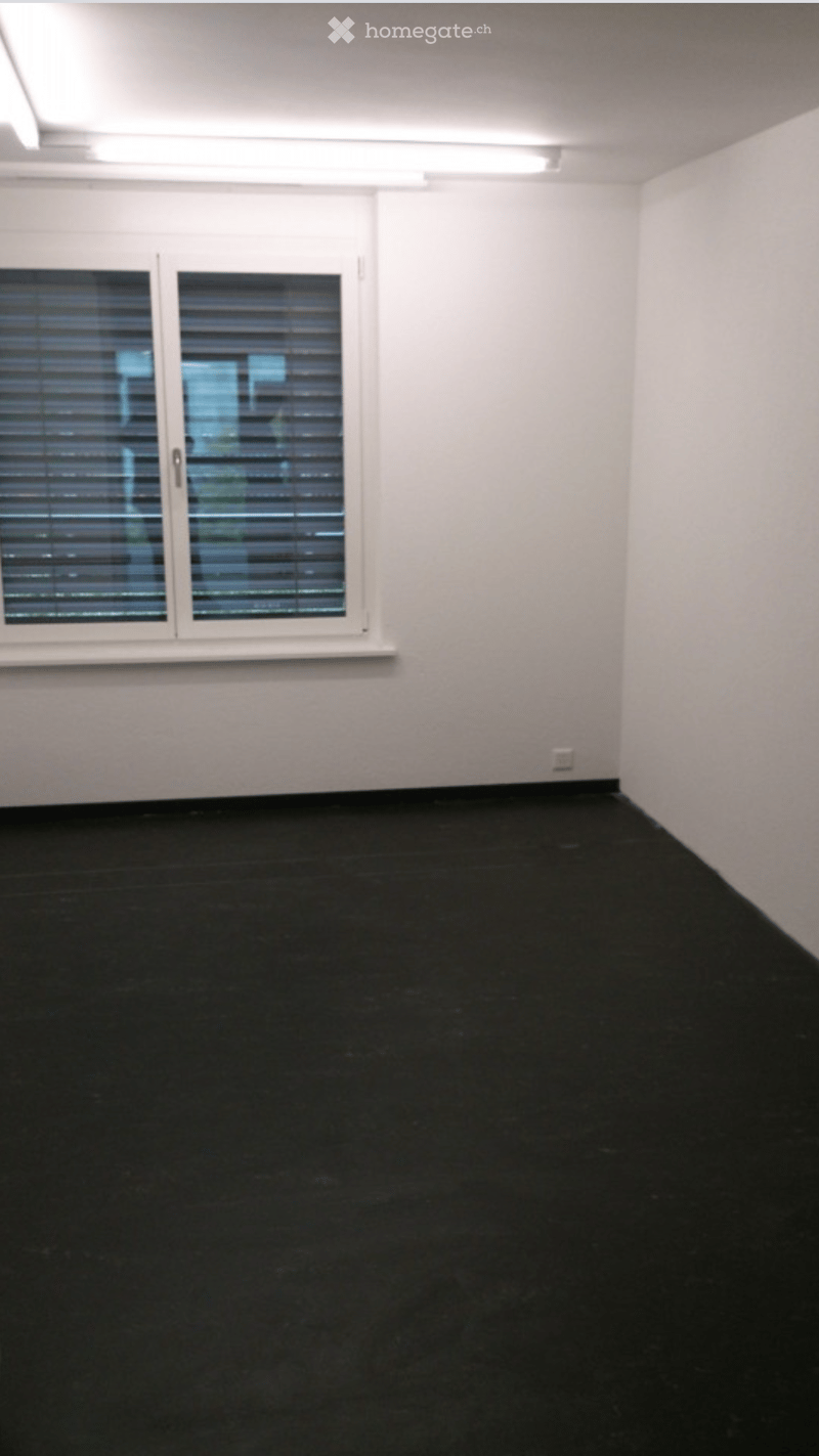 Empty room with white walls, black flooring, and a large window with blinds.