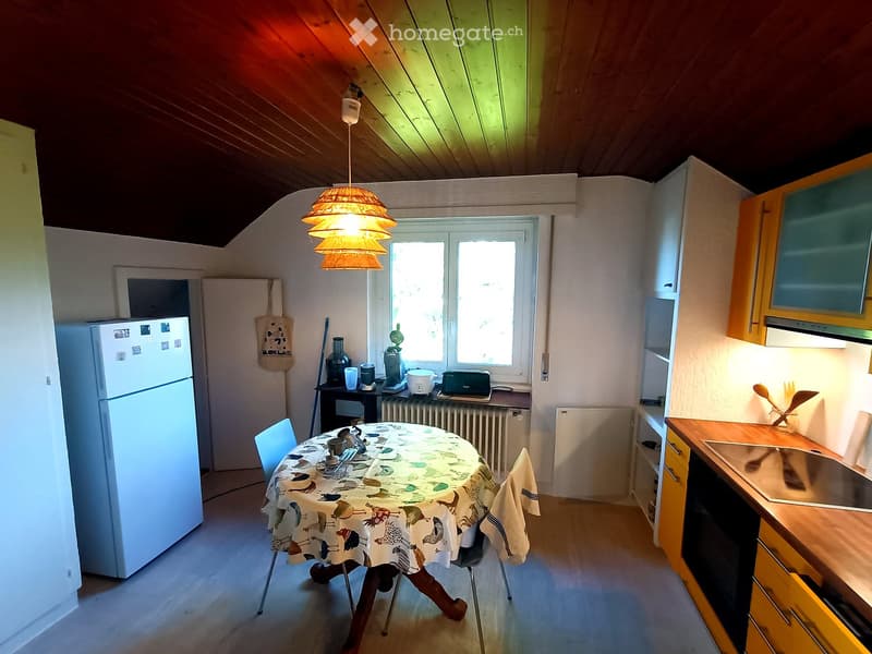 Bright kitchen with wooden cabinets, a dining table with chairs, a refrigerator, and various appliances including a toaster and a sink.