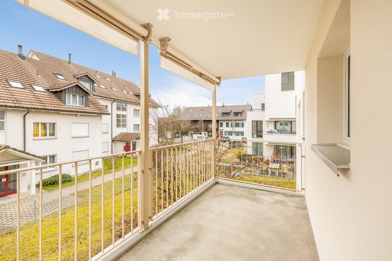 Balcony with metal railing, retractable awning, and view of residential area with houses and greenery.