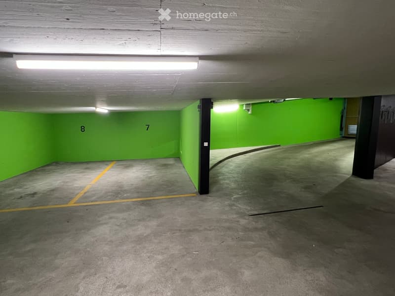 Empty underground parking garage with green walls, concrete floor, and numbered parking spaces.