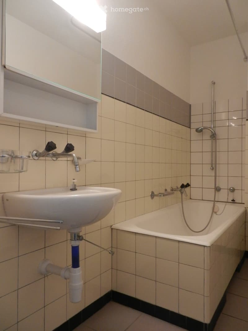 Bathroom with a sink, bathtub, and mirror. The walls are tiled with a light beige color and a darker border at the bottom.