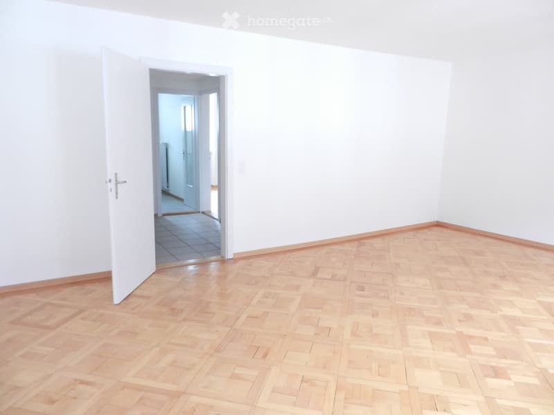 Empty room with wooden flooring and white walls, featuring an open doorway leading to another tiled area.