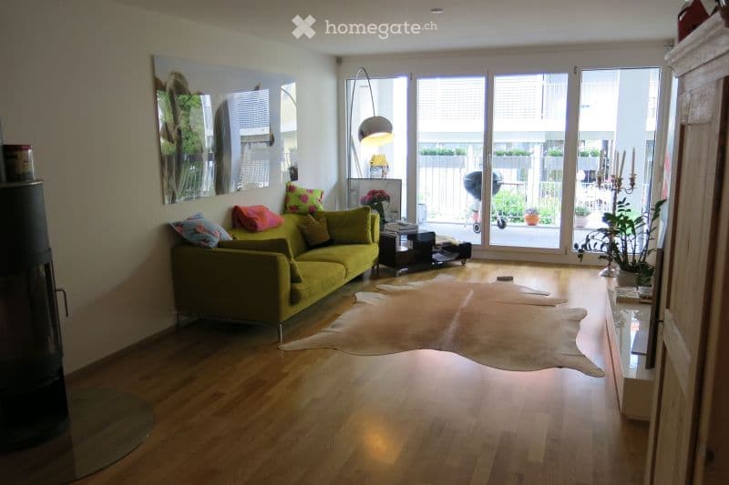 Bright living room with large windows and a balcony, featuring a green sofa, coffee table, floor lamp, and decorative mirror.