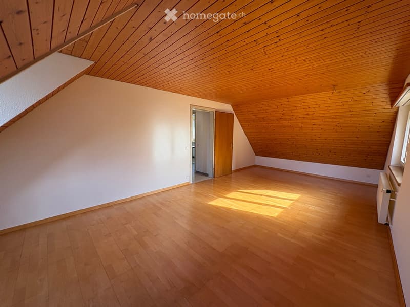 Empty room with wooden flooring and slanted wooden ceiling, featuring a doorway leading to another room.