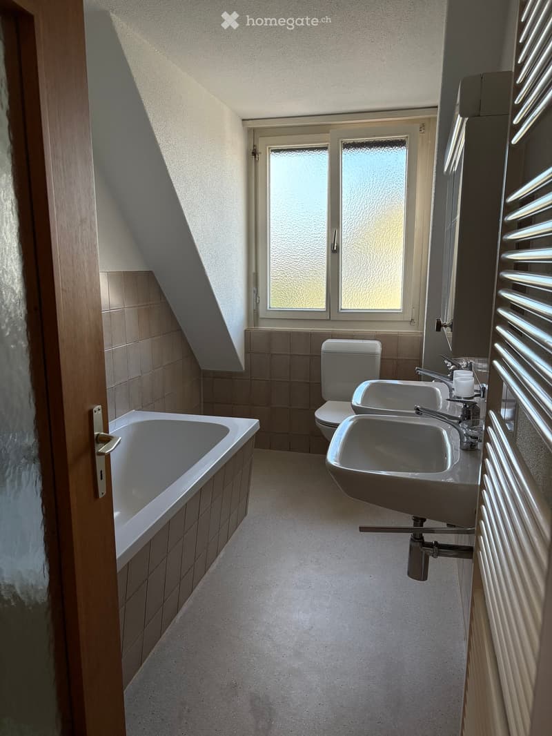 Bathroom with a bathtub, toilet, sink, and radiator. The room has a sloped ceiling and frosted windows.