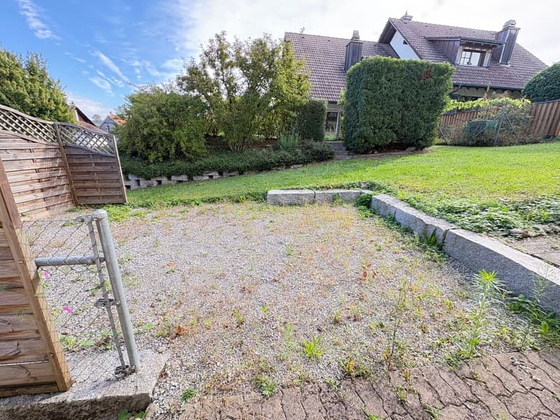 Garden area with gravel pathway, wooden fence, stone steps, and a house with a tiled roof in the background.