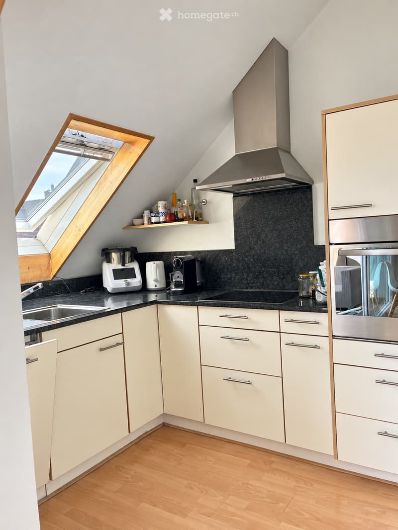 Modern kitchen with light-colored cabinets, stainless steel appliances, and a black countertop. Features include a built-in oven, microwave, coffee maker, and a window with wooden frame.