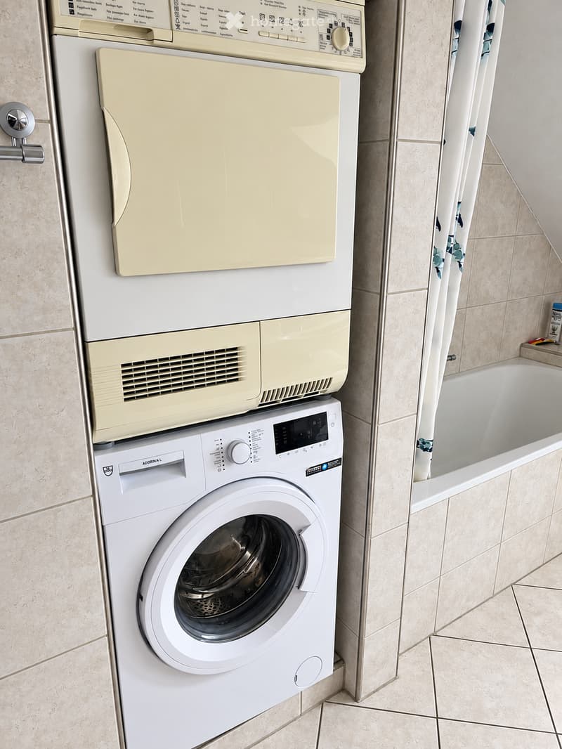 Bathroom with a washing machine and dishwasher stacked vertically, a bathtub, and tiled walls.