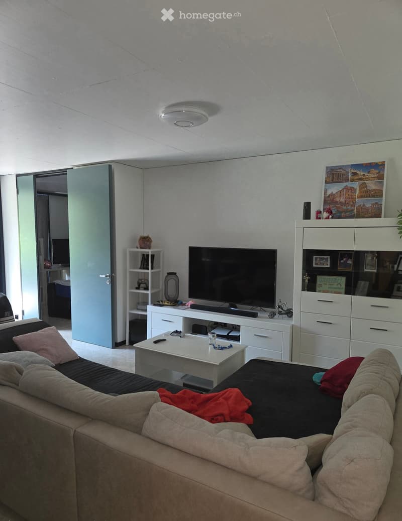 Modern living room with a beige sofa, coffee table, television, white cabinet, and shelves. The room features a sleek design with a mix of contemporary and minimalist furniture.