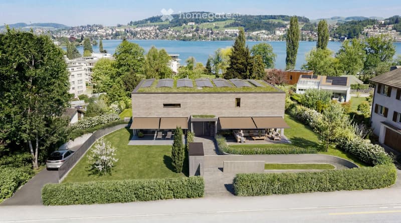 Modern house with a green roof, surrounded by a well-maintained garden, overlooking a lake and distant hills.