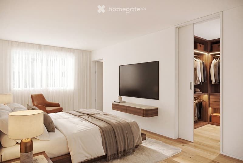 Modern bedroom with a large bed, nightstand, lamp, armchair, wall-mounted TV, and built-in wardrobe with lighting.