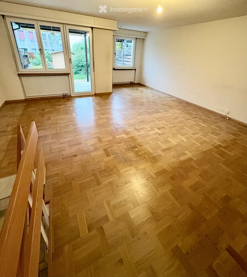 Empty room with wooden flooring, large windows, and a sliding glass door leading to a balcony.