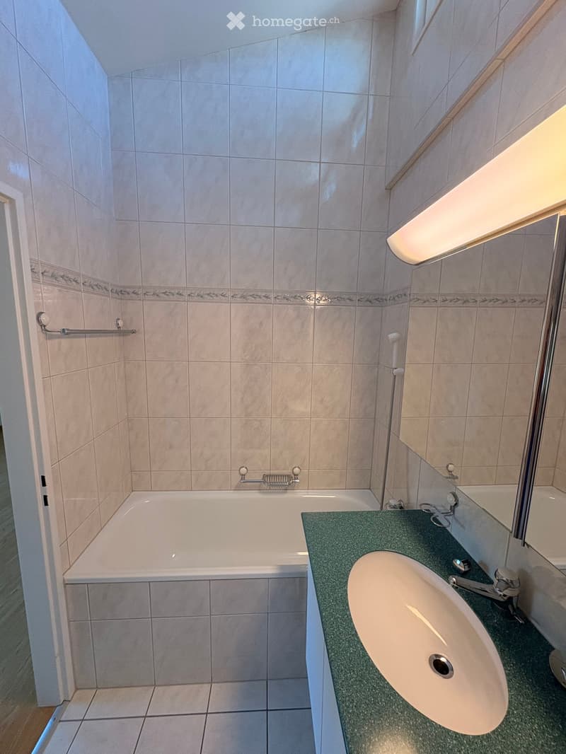 Bathroom with a bathtub, sink, and handrail, featuring tiled walls and a window with blinds.