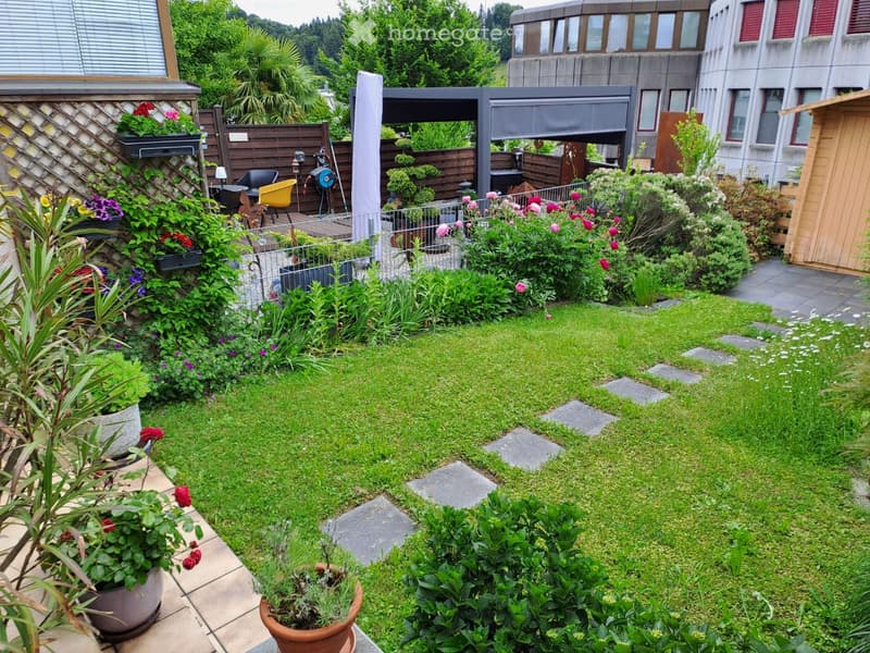 Well-maintained garden with a lawn, potted plants, and a small patio area with outdoor furniture.