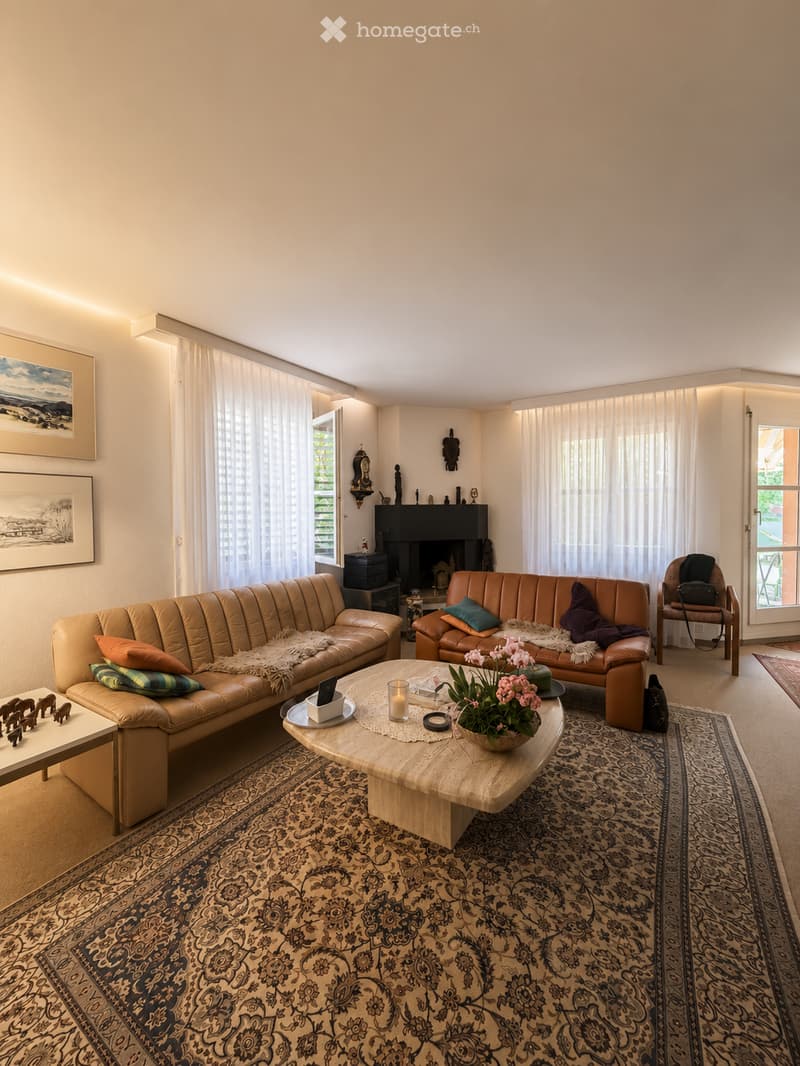 A well-lit living room with two leather sofas, a coffee table, an armchair, a fireplace, and decorative items including a flower vase and picture frames.