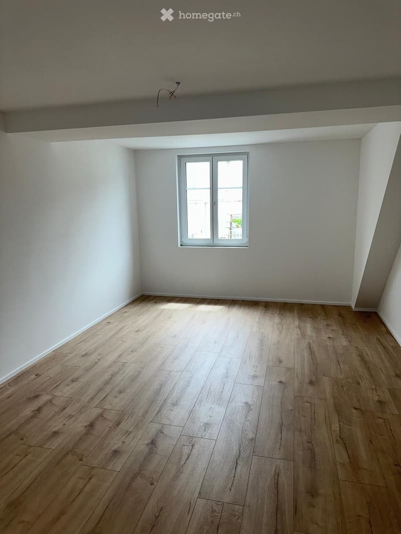 Empty room with wooden flooring and white walls, featuring a single window with white frame and glass panels.