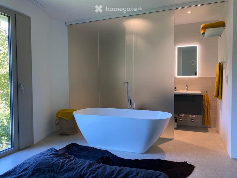 Modern bathroom with a freestanding bathtub, sink, illuminated mirror, and towels.