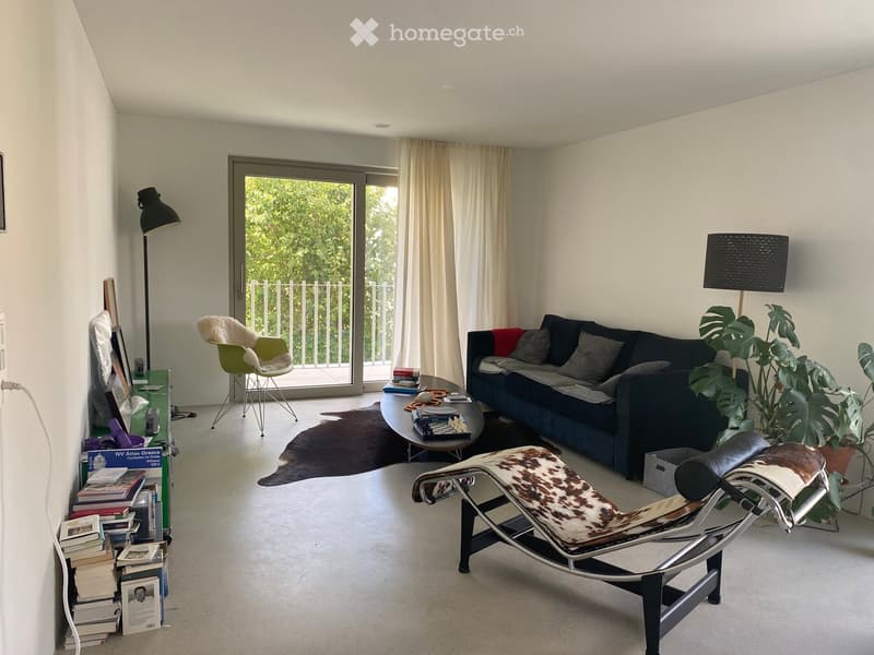 Modern living room with white walls, large sliding glass doors leading to a balcony, a dark blue sofa, a round coffee table, a white armchair, a floor lamp, a lounge chair, and a potted plant.