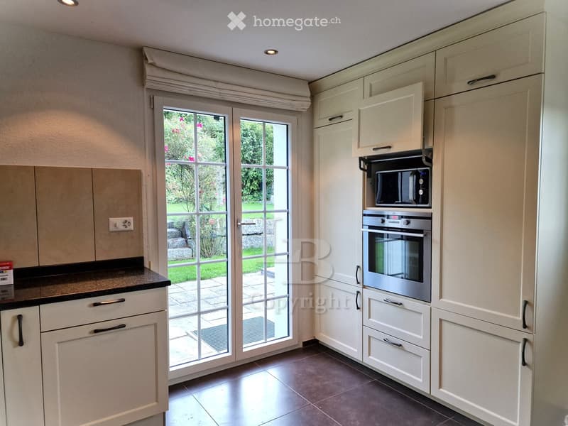 Modern kitchen with cream cabinets, stainless steel appliances, and a large glass door leading to a garden.
