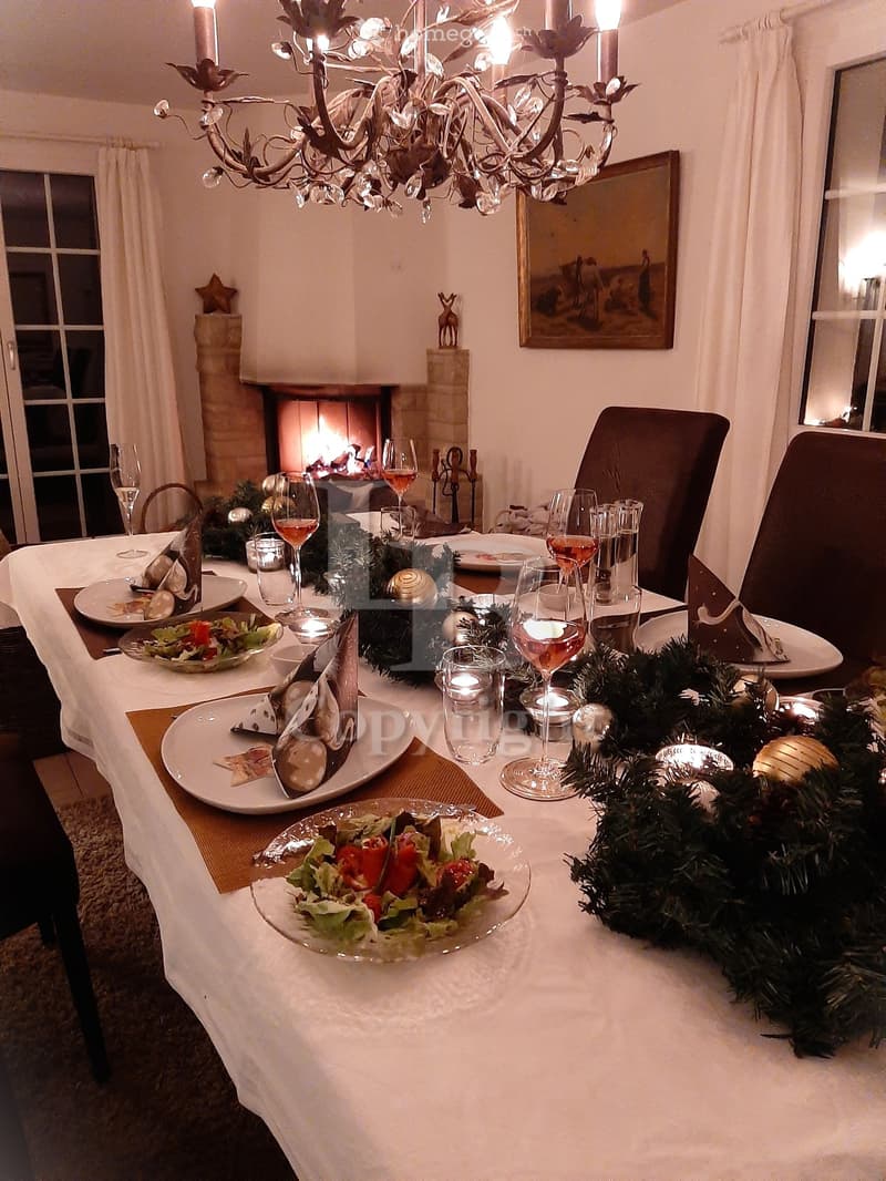Elegantly set dining table with plates, wine glasses, and candles, surrounded by a festive garland, with a fireplace in the background.