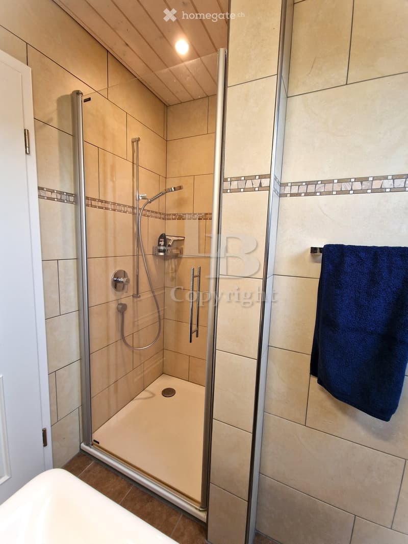 Modern bathroom with a glass-enclosed shower, beige tiles, a bathtub, and a dark blue towel hanging on a rack.