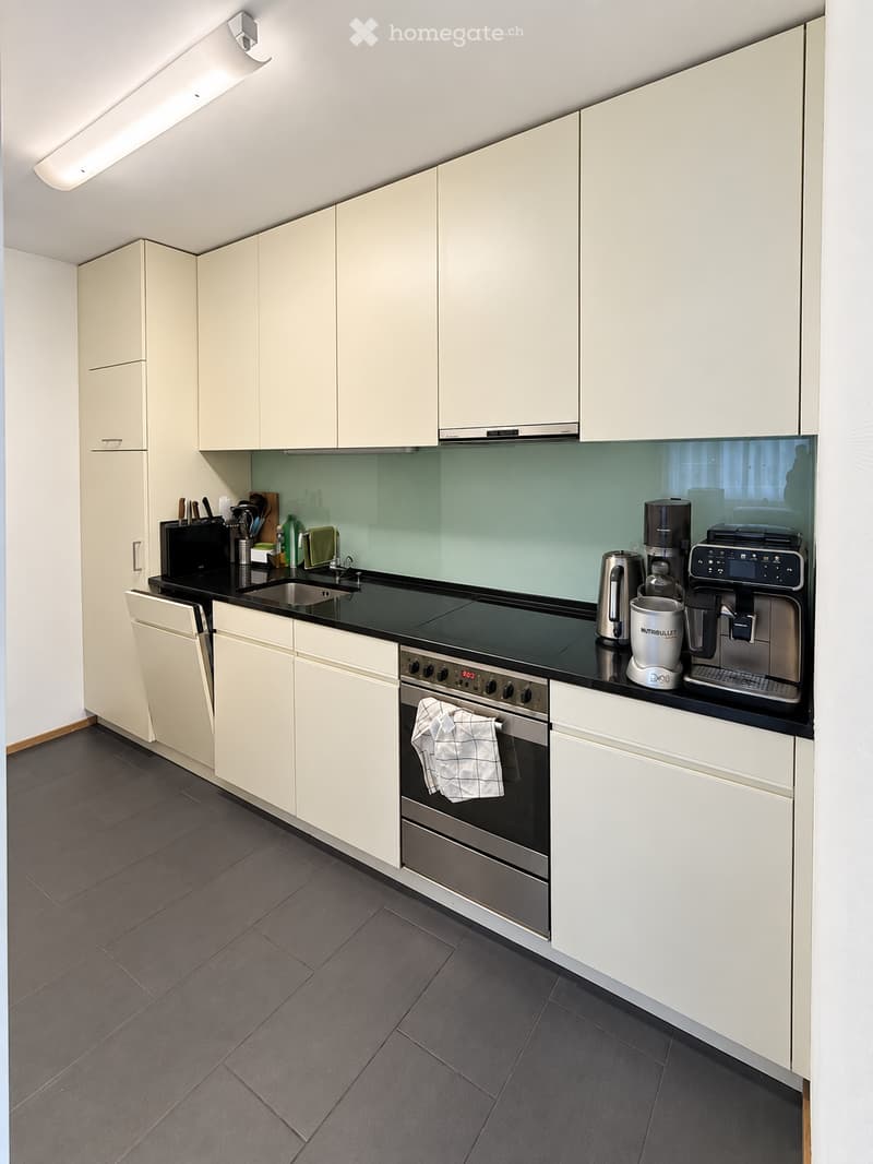 Modern kitchen with white cabinets, black countertops, stainless steel appliances, and a dark tiled floor.