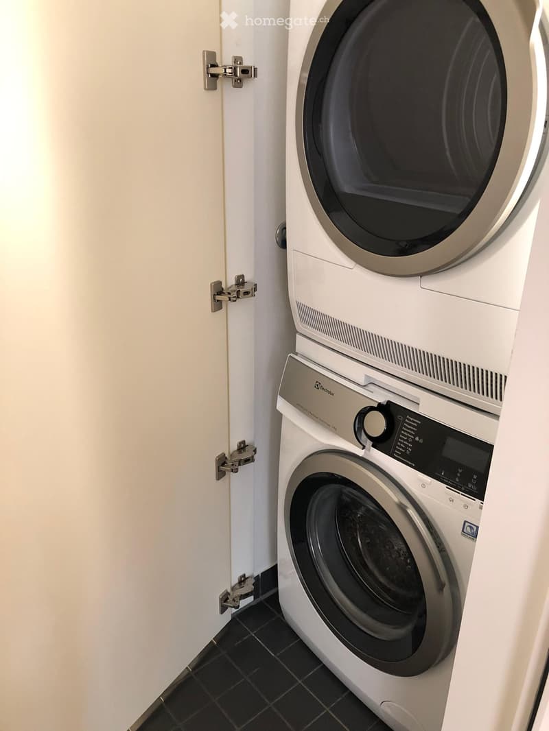 A modern bathroom with a white washing machine and dryer unit, featuring a sleek design and digital control panel.