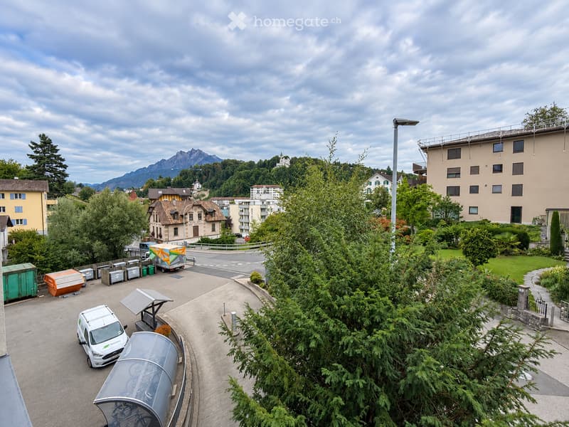 A view of a residential area with trees, parked vehicles, and buildings, with mountains in the background.