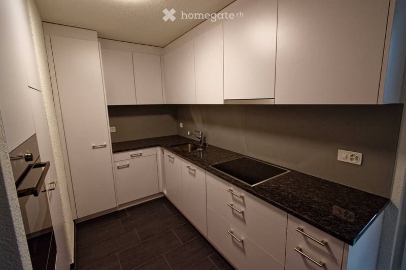 Modern kitchen with white cabinets, dark granite countertops, and stainless steel appliances including a sink, faucet, and stove.