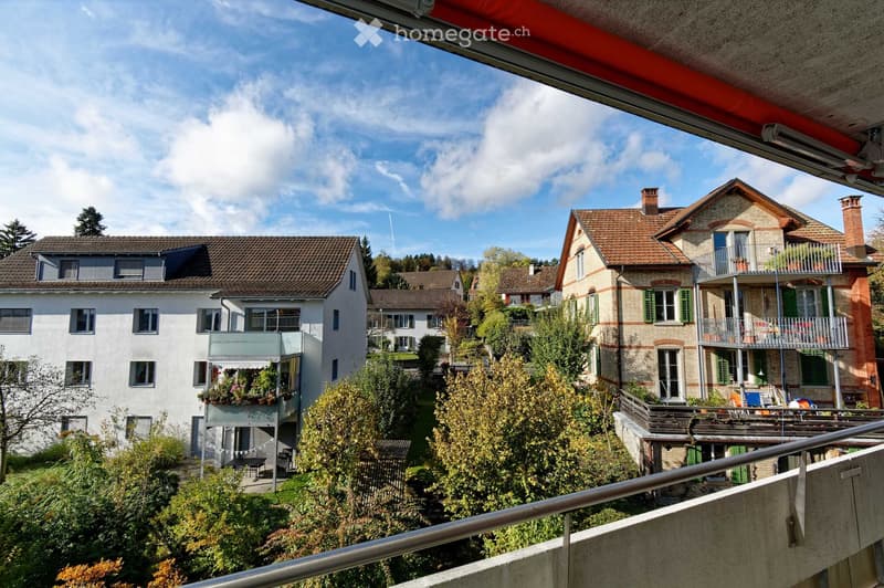 View from a balcony overlooking a residential area with multiple houses, balconies, and greenery.