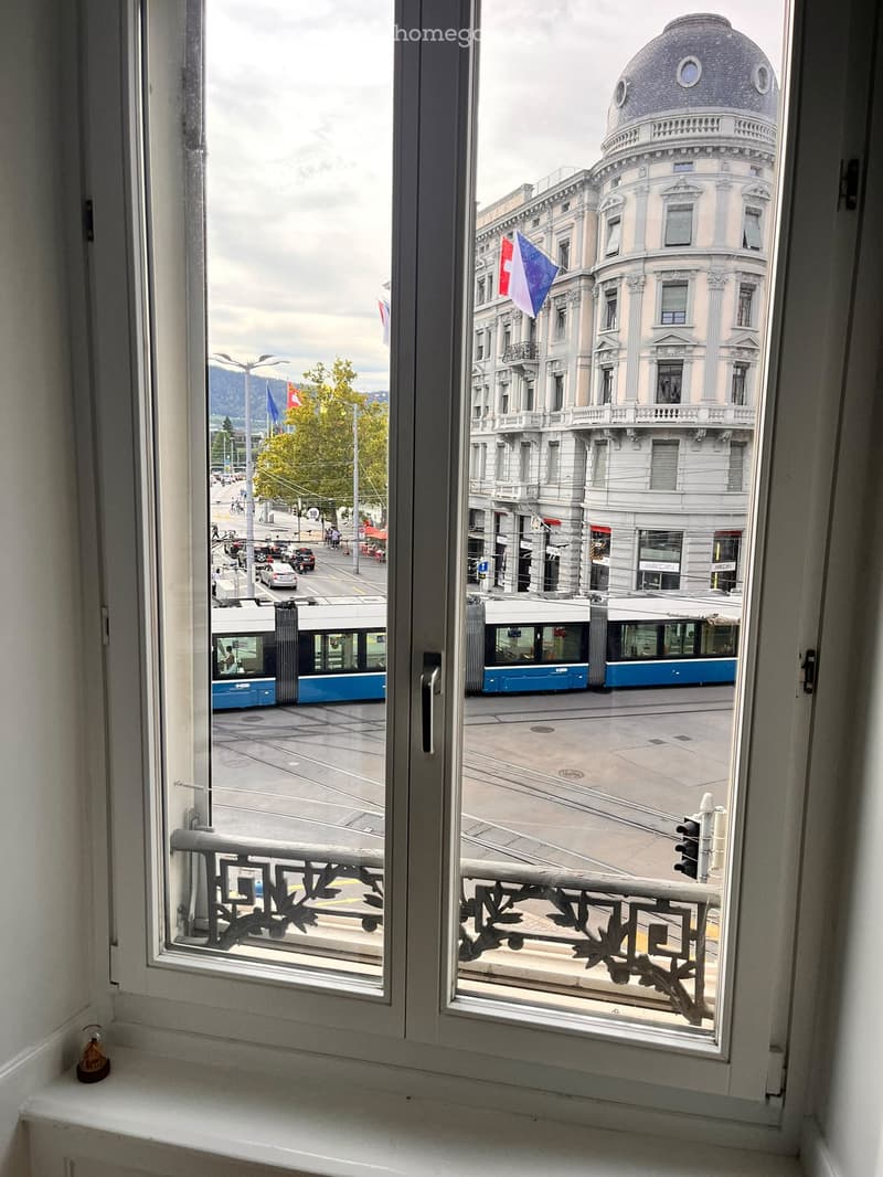 Balcony overlooking a city street with a tram, a domed building, and a Swiss flag.