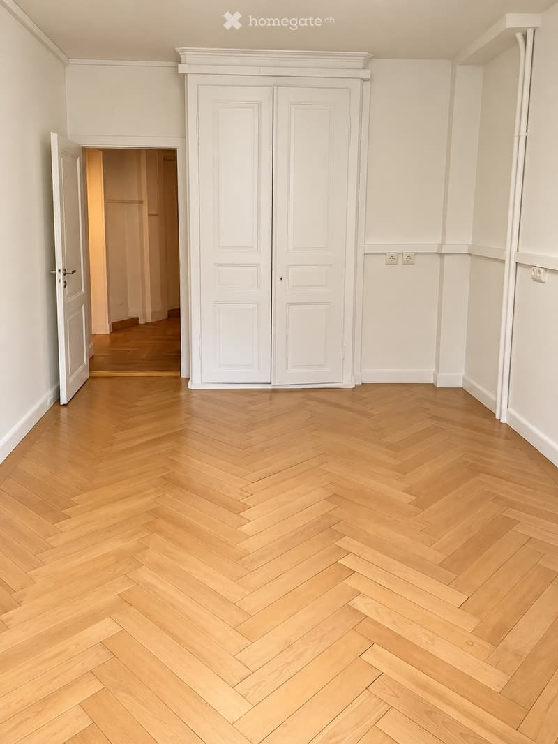 Empty hallway with herringbone-patterned wooden flooring, white walls, and double doors.