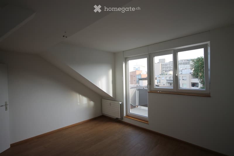 Empty room with wooden flooring, white walls, large windows, and a radiator. No furniture or equipment present.