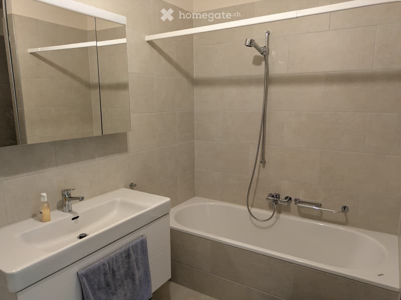 Modern bathroom with a white sink, bathtub, mirror, and towel. Beige tiles and a sleek design.