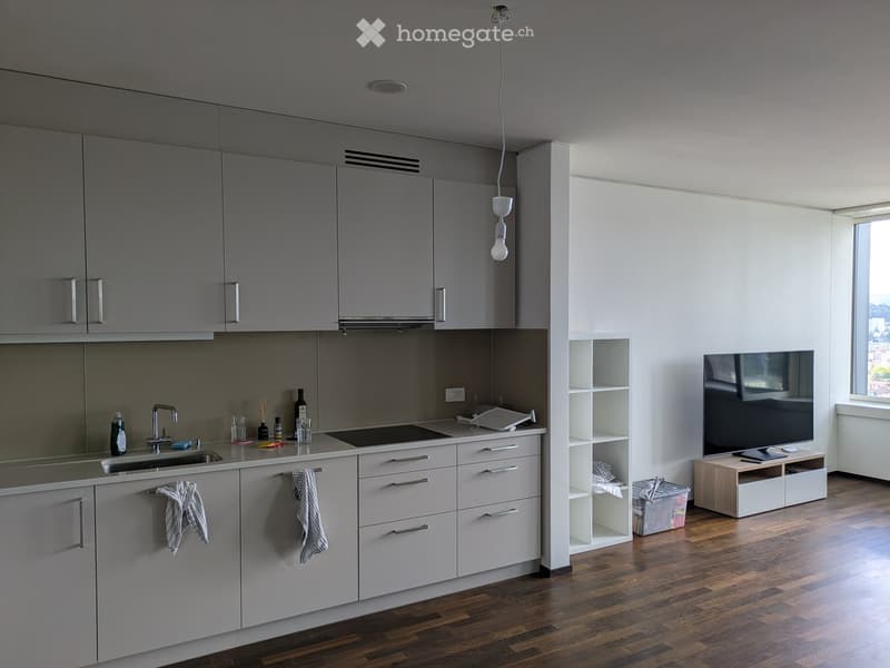 Modern kitchen with grey cabinets, a central island, and a television on a stand. The space features wooden flooring and white walls.