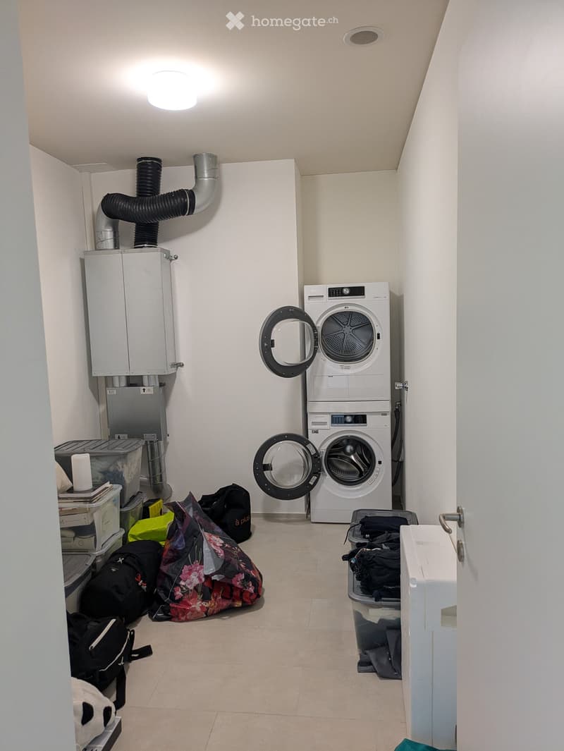 Laundry room with a washing machine, dryer, water heater, and storage bins. Several bags and luggage are placed on the floor.