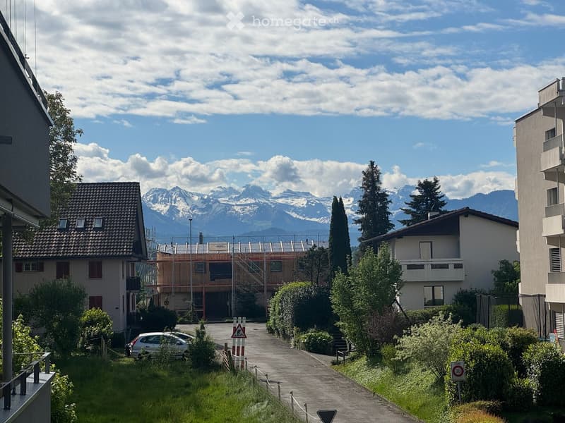 Residential area with multi-story buildings, a parked car, and a scenic mountain backdrop.