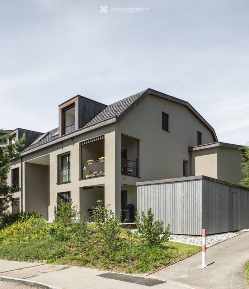 Modern two-story house with a flat roof, large windows, and a balcony with potted plants.