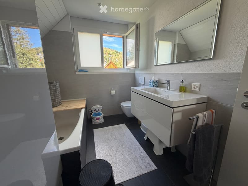 Modern bathroom with a bathtub, sink, toilet, and a small child's potty. Features a large mirror, towel rack, and a view of the outdoors through a window.
