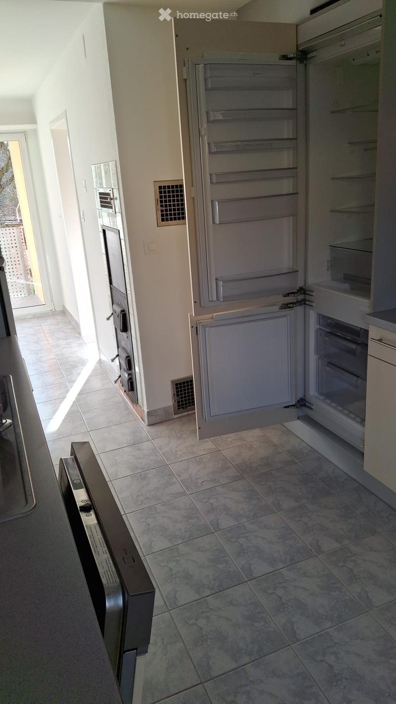 Modern kitchen with tiled floor, open refrigerator, and built-in oven. Natural light from the balcony entrance.