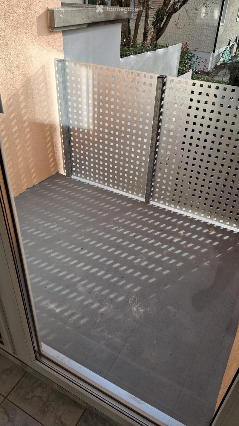Balcony with concrete floor, glass and metal lattice screens, and visible shadows from the lattice pattern.