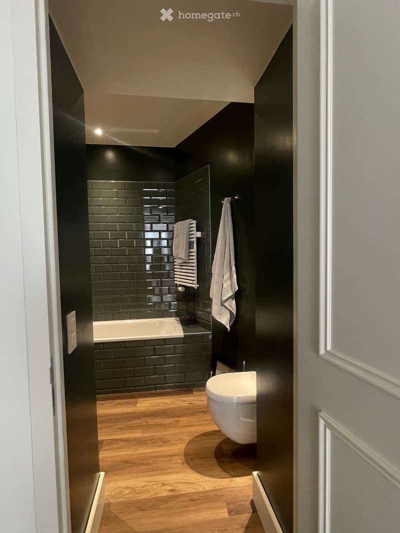 Modern bathroom with dark walls, wooden floor, bathtub, sink, towel, and radiator.