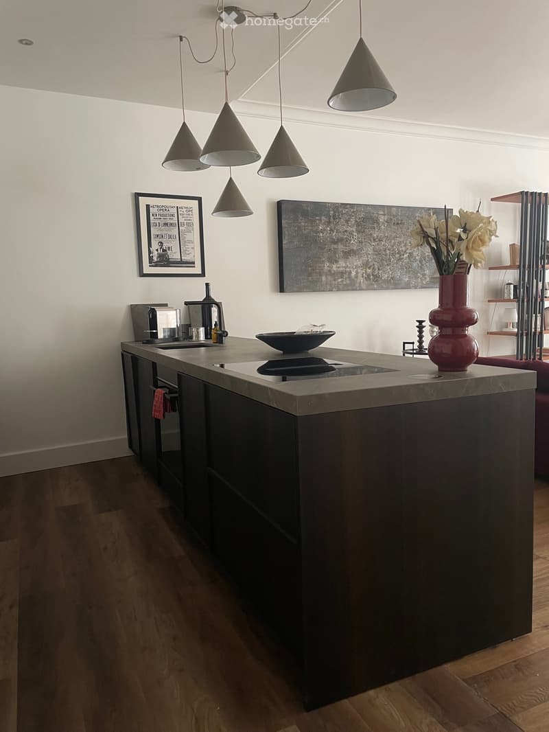 Modern kitchen with a dark wooden island, pendant lights, a sink, coffee maker, and decorative vase on the counter.