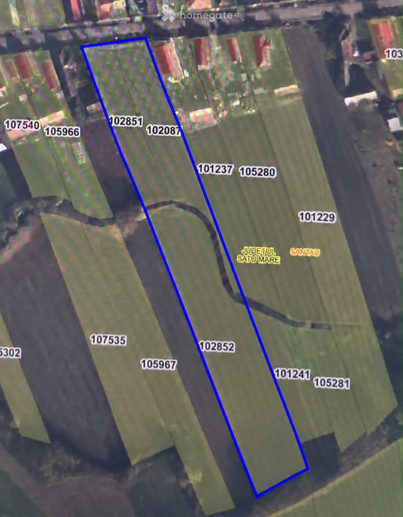 Aerial view of a rural area with multiple plots marked by numbers, surrounded by green fields and small structures.