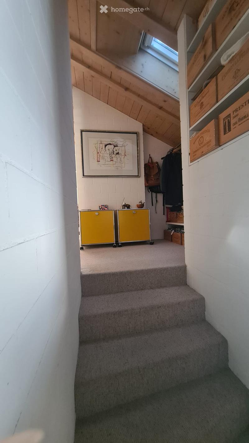 Carpeted staircase leading up, with wooden slanted ceiling, white brick walls, small yellow cabinets, artwork, and storage boxes on shelves.