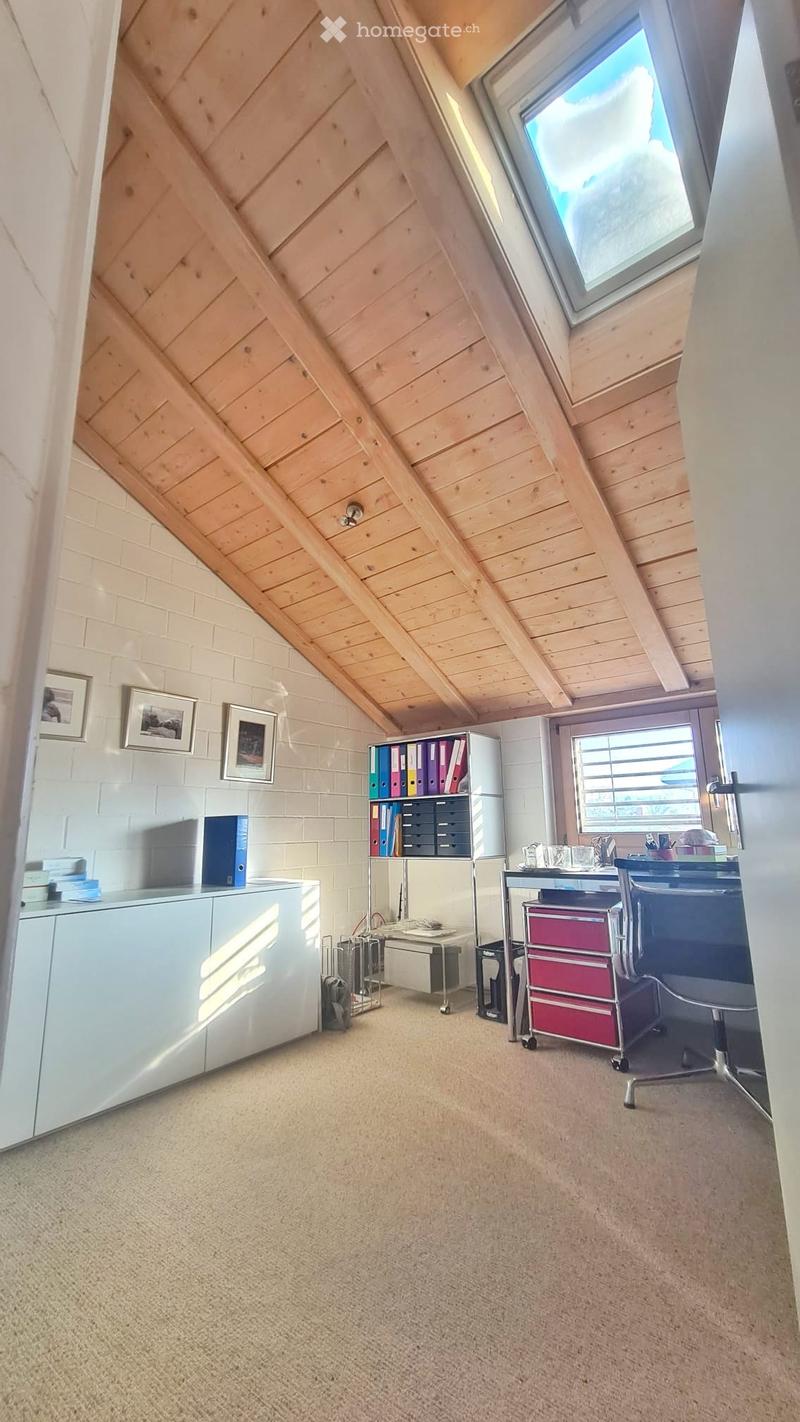 Bright attic office with wooden slanted ceilings, large windows, and modern furniture including a desk, chair, filing cabinet, and cabinet.