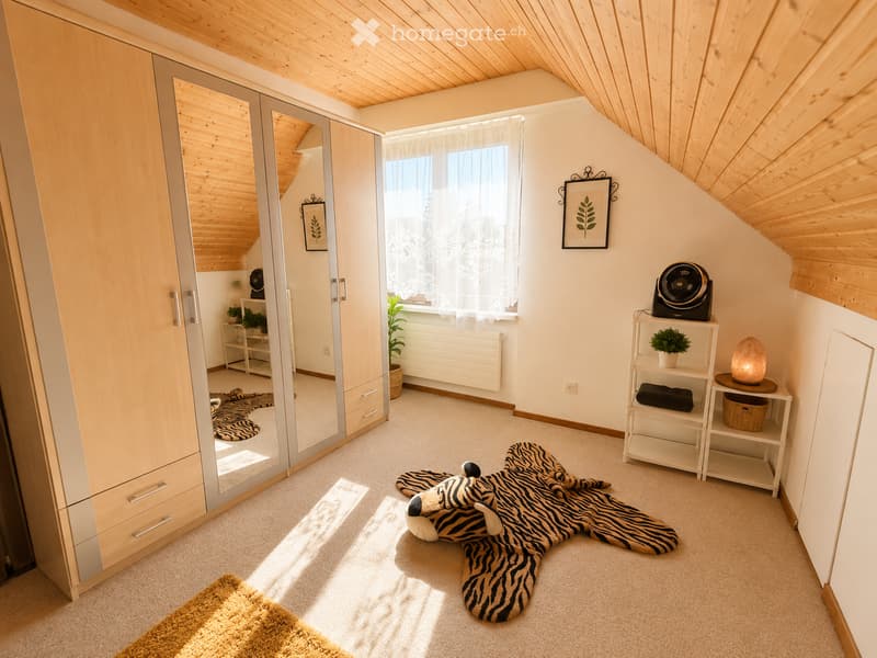 Bright, cozy bedroom with wooden slanted ceiling, large window with white curtains, wardrobe with mirrored doors, small shelf with plant and fan, and a large stuffed animal on the floor.