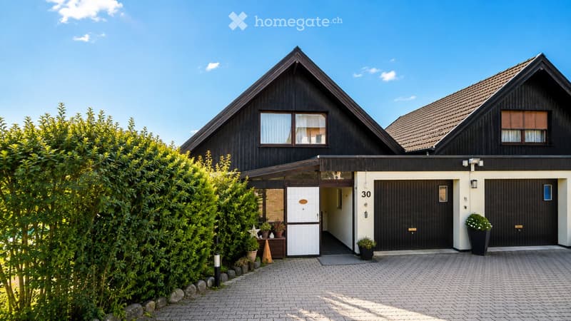 Two-story house with dark wooden exterior, white garage doors, and a small entrance area with potted plants.