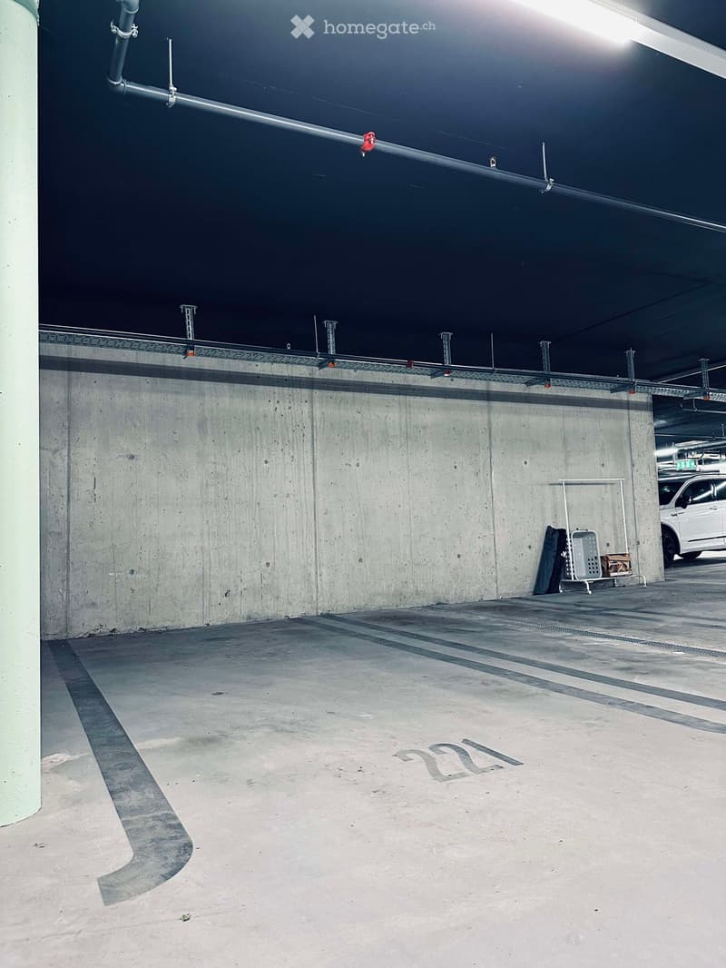 Empty underground parking space with concrete walls, floor markings, and a single parked car visible in the background.